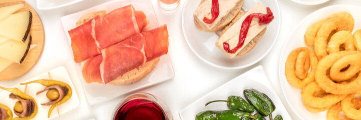 A panorama of Spanish tapas. Jamon, squid rings, cheese, gildas and other snacks, shot from the top on a white background