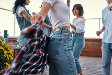 Close up photo of a woman in casual clothes holding checkered shirt behind back while standing on rooftop terrace with her friends