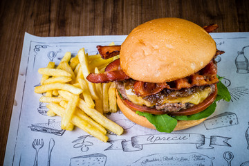 Craft beef burger with cheese, bacon, rocket leafs, caramelize onion and french fries on wood table and rustic background.