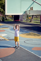 Full-length photo of athlete man throwing ball into basketball hoop on playground.