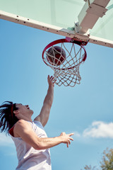 Image of athlete man throwing ball into basketball hoop on sports field on street on summer day.