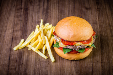 Craft beef burger with cheese, italian peperoni, tomato, basil leafs and french fries on wood table and rustic background.