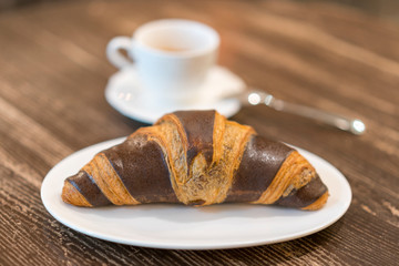 Fresh and tasty croissants with chocolate and cup of coffee on wooden background. copy space