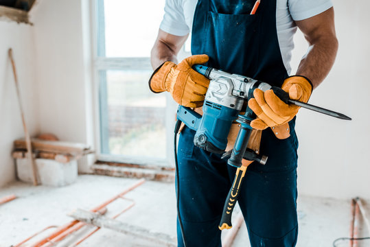 cropped view of workman in yellow gloves holding hammer drill