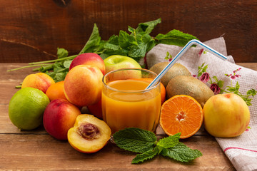 Fruits lie on a wooden table. In the center is a glass of fruit juice.