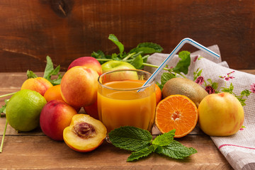 Fruits lie on a wooden table. In the center is a glass of fruit juice.