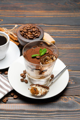 Portion of Classic tiramisu dessert in a glass, cup of coffee and savoiardi cookies on wooden background