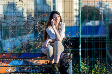 Portrait of a happy woman sitting on the bench and talking on the phone outdoors