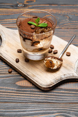 Portion of Classic tiramisu dessert in a glass cup on cutting board on wooden background