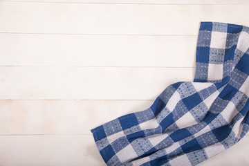 A blue checkered cotton tablecloth lies on a wooden background. Flat lay. Copy cpaes.