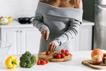 cropped view of woman holding knife near red cherry tomatoes and fruits