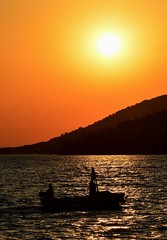 Silhouette of fishing boat and two fisherment during their sunset evening return in Croatian bay near Paklenica national park.
