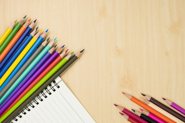 Obraz premium colorful pencils and notebook on wooden background top view. art equipment.