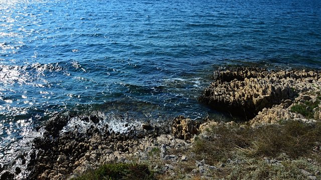Mild waves of Adriatic sea breaking on rocky shore in afternoon summer sunshine, north of Vrsi village, Zadar district, Croatia.