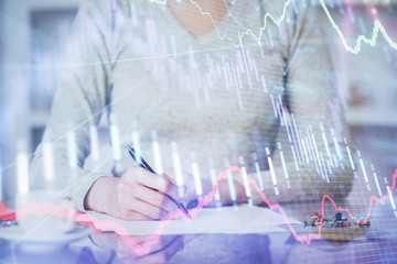 Hand taking notes in notepad. Forex chart holograms in front. Concept of research. Multi exposure