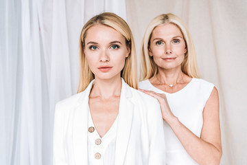 elegant blonde smiling mother and serious daughter in total white outfits