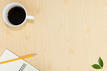 Top view of notebook pencil and cup of coffee on wood table background.Business desk minimal style concept with copy space for any design.Flat lay.