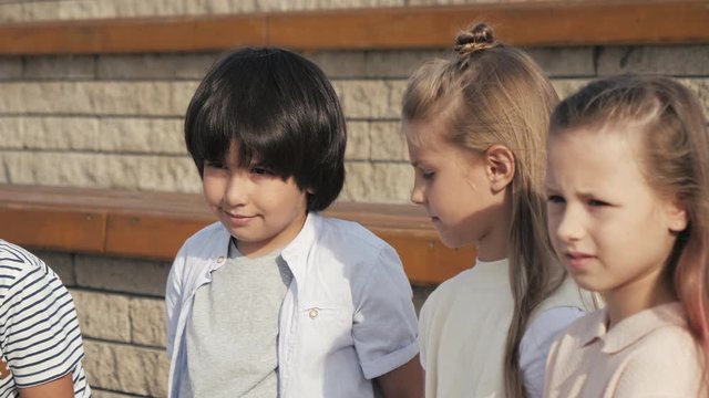 Diverse group of kids sitting on a bench together waiting.