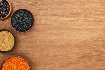 top view of bowls with beans, red lentil, and cereal on wooden surface