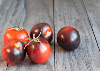 Black little cherry tomatoes on wooden background. Varietal tomato rich in anthocyanins.