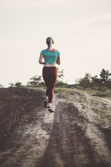back of young woman in sportswear running distance in the field, girl engaged in sport outdoors, concept healthy lifestyle