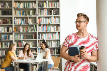 Young man with books and drink in library. Space for text