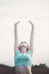young woman doing breathing exercises in nature, taking a deep breath raising her head and arms up, girl is engaged in fitness outdoors, concept sport and healthy lifestyle