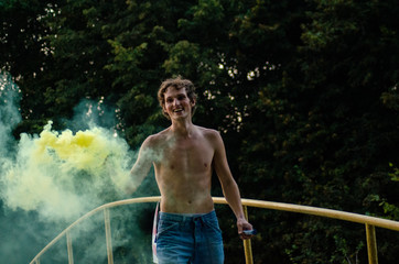 a young man in a blue jumpsuit and a white T-shirt is holding a smoke bomb in his hands. A man is holding colored orange smoke
