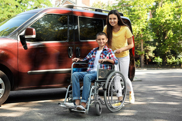 Young woman with boy in wheelchair near van outdoors