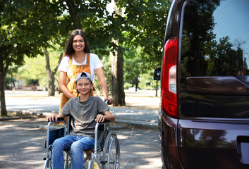 Young woman with boy in wheelchair near van outdoors © New Africa