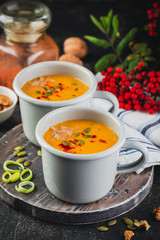 Pumpkin soup in a metal mugs on a wooden board