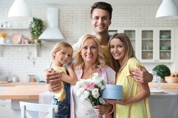 Portrait of happy family with bouquet and gift box in kitchen