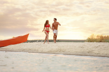 Happy young couple running together on sea beach at sunset