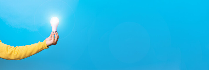 idea solar energy, hand holding light bulb, illuminated light bulb, panoramic mock up over blue...