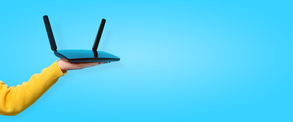 black wifi router on hand over blue background, panoramic mock up image
