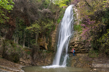 Fototapeta na wymiar A girl stands next to a waterfall in the Tbilisi Botanical Garden