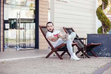 Fototapeta na wymiar Thoughtful young stylish hipster man with beard resting sitting on the lounge beside the hotel. Concept of long-awaited vacation