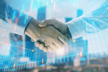 Double exposure of financial graph on cityscape background with two businessman handshake. Concept of stock market deal