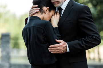 cropped view of sad elderly man embracing woman on funeral - obrazy, fototapety, plakaty