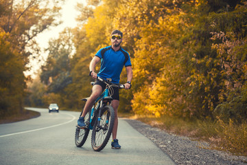 Naklejka premium Happy bearded man cyclist rides in the sunny forest on a mountain bike. Adventure travel.