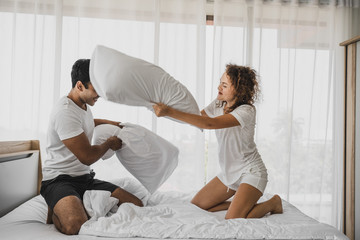 a man and a woman playing pillow on the bed