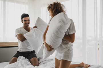 a man and a woman playing pillow on the bed