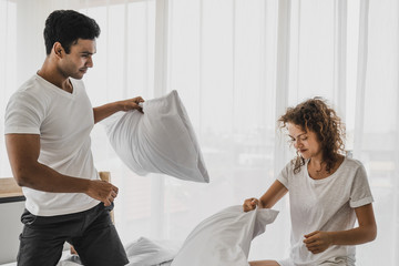 a man and a woman playing pillow on the bed