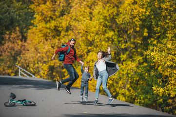 Happy family of three jumping on rural road in solar autumn day.