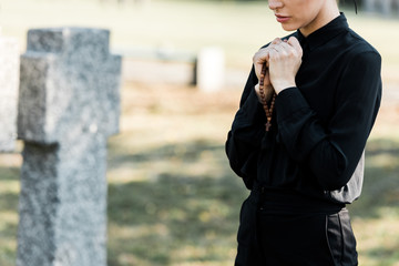cropped view of woman holding rosary beads near tombstone