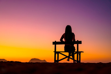 Fototapeta na wymiar Lifestyle A girl in a beautiful sunset sitting in a chair with her legs crossed looking to the left. Copyspace