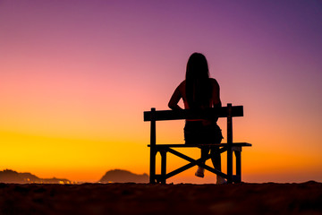 Fototapeta na wymiar Lifestyle A girl in a beautiful sunset sitting on a chair with her legs crossed. Copyspace