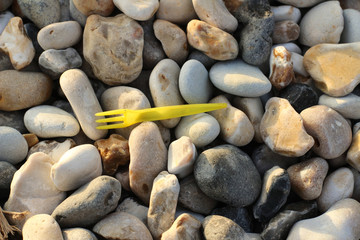 Plastic fork on pebbles at the beach, environment and ocean pollution
