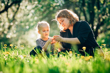 Naklejka na ściany i meble Mother and daughter having fun in the park. Happiness and harmony in family life. Beauty nature scene with family outdoor lifestyle. Woman and cheerful little girl