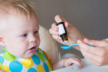 vitamins for young children. mom drips vitamins into a spoon while feeding her little son. healthy childhood. fortification and protection against diseases at an early age